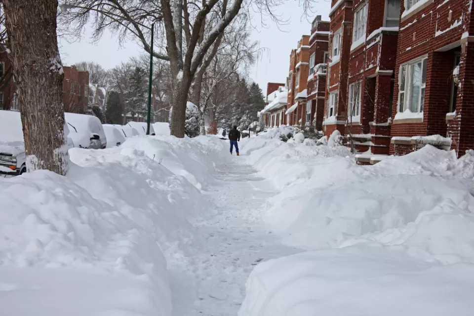 Snow-covered Chicago sidewalk with piles of snow on either side and red brick homes on the right